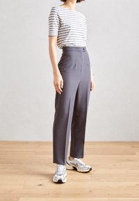 Pantalon gris taille haute avec plis latéraux, associé à un haut à manches courtes rayé gris clair et blanc, et des chaussures de sport argentées.