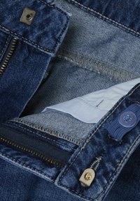 Temno modro denim blago z vidnim zadrgo in gumbom za zapiranje, ki ima svetlo modro podlogo. Tekstura tkanine je gladka in trdna.