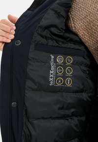 Schwarze isolierte Jackeninnenseite mit einer wasserdichten und atmungsaktiven Membran, mit Symbolen für Wasserbeständigkeit, Winddichtigkeit und geklebten Nähten.