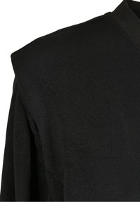 Tissu noir tricoté montrant un gros plan d'une épaule avec un détail matelassé ou structuré sur un vêtement.