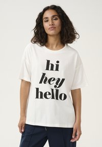 T-shirt bianco in cotone con grande testo nero che dice "hi hey hello". Vestibilità ampia, scollatura rotonda e maniche corte.
