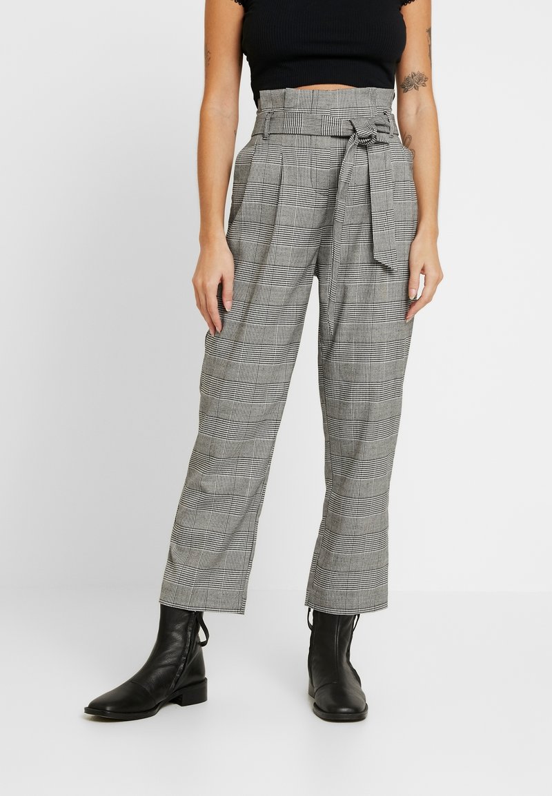 Pantalon à carreaux gris à taille haute, jambes larges, avec une ceinture à nouer. Porté avec des bottines noires en cuir lisse.