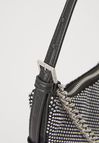 Black handbag featuring a textured surface with silver studs, a chain strap, and a rhinestone-accented buckle for adjustable wear.