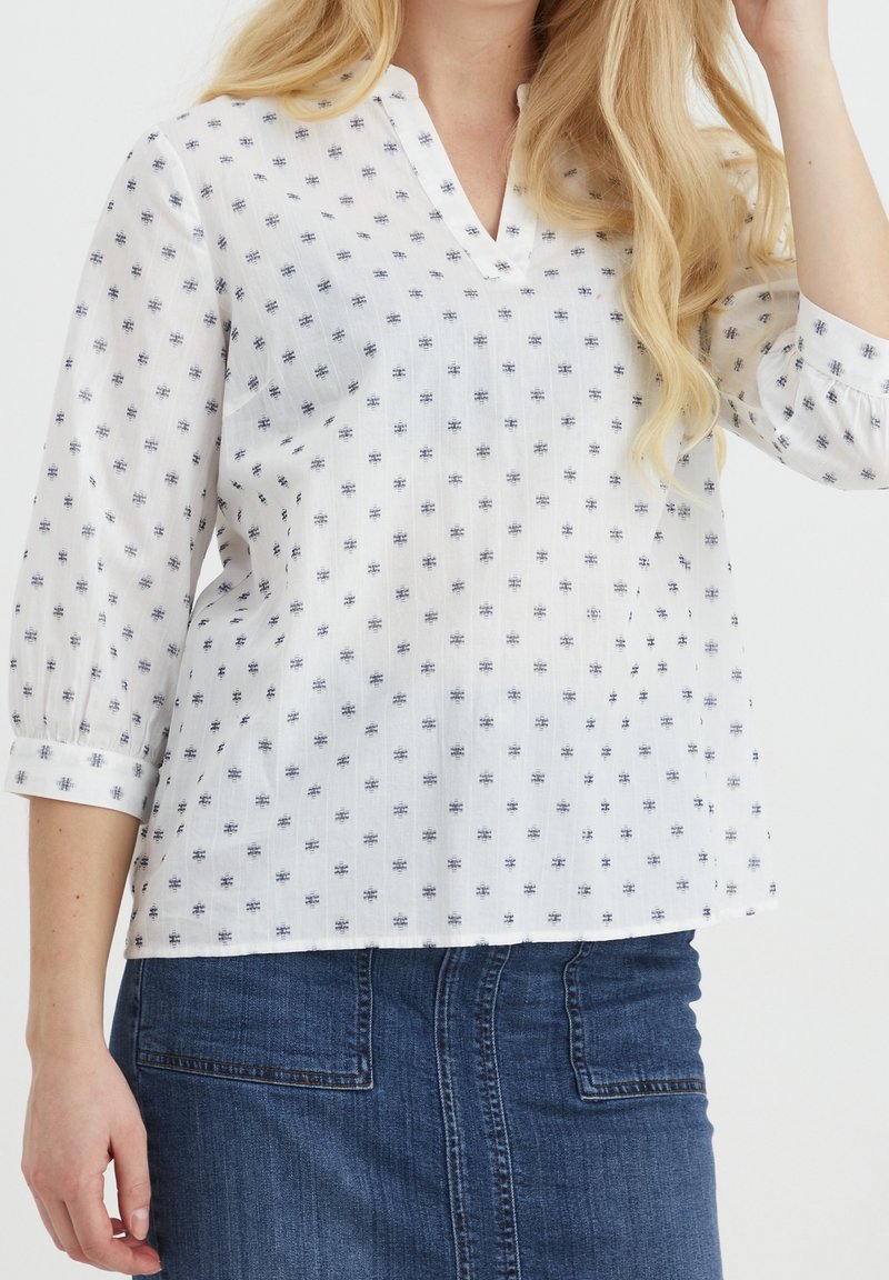 Blusa bianca con stampa navy, dotata di scollatura a V e maniche a tre quarti. Il tessuto è leggero con una finitura testurizzata.