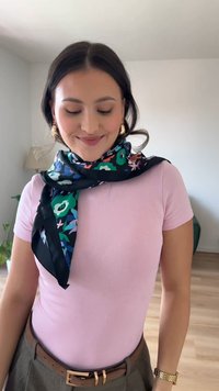 Svila šal z rožnatim vzorcem v zelenih, modrih in roza odtenkih, obdan z črnim robom. Oblečen okoli vratu čez svetlo roza majico.