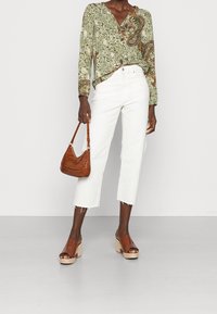 Grünbluse mit langen Ärmeln und Paisleymuster, weiße Cropped-Jeans, braune strukturierte Handtasche und braune Plateausandalen mit offener Zehe.