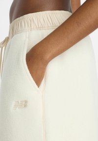 Witte fleece joggingbroek met een beige elastische tailleband, voorzien van een zijzak en een klein geborduurd logo in een bijpassende kleur.