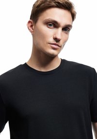 Black crew-neck t-shirt with a ribbed texture, fitted design, and short sleeves. The fabric appears smooth and soft against a light background.