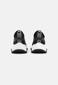 Schwarz-weiße Sportschuhe mit einem Obermaterial aus Mesh, dicker weißer Zwischensohle, strukturierten schwarzen Laufsohlen und einem Zugband mit Markenlogo-Detail.