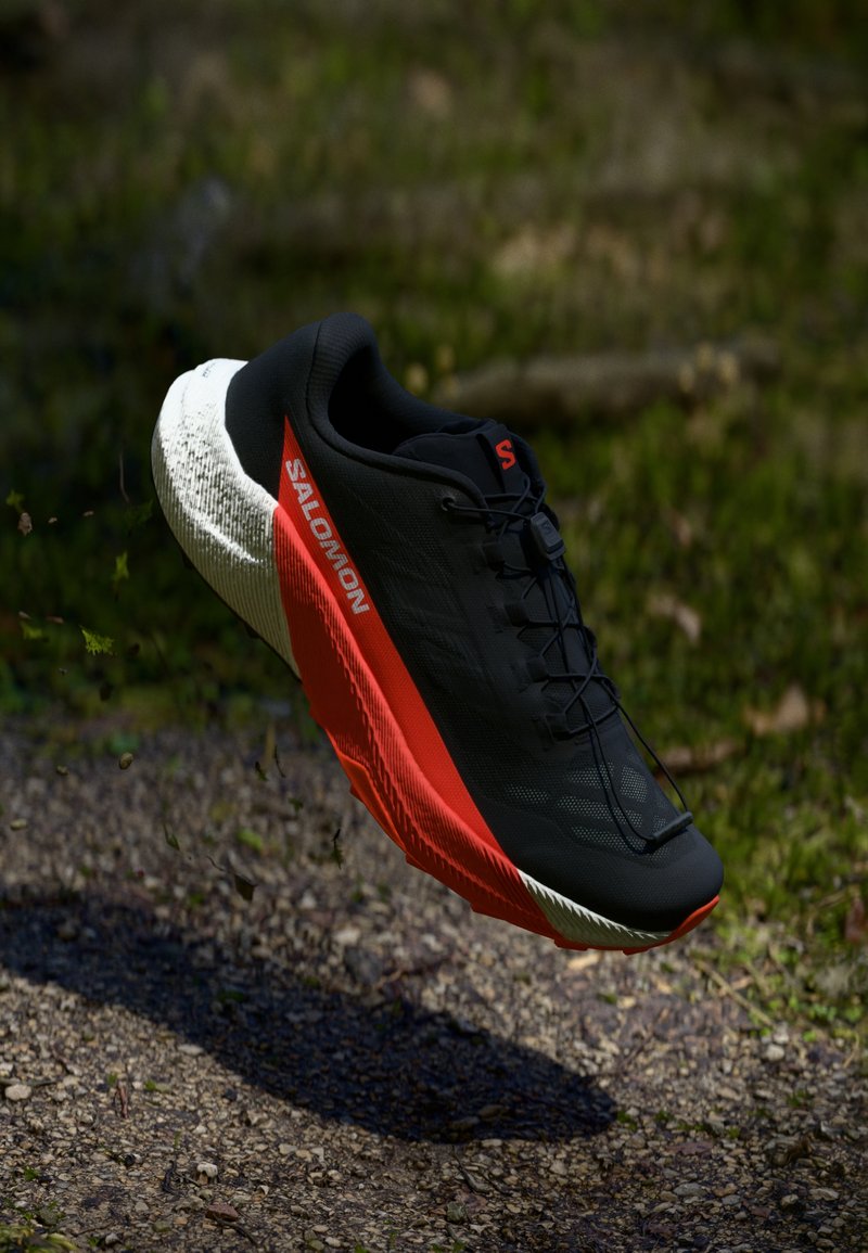 Black running shoe with red accents, lightweight mesh upper, textured white sole, and lacing system. Designed for performance and comfort.