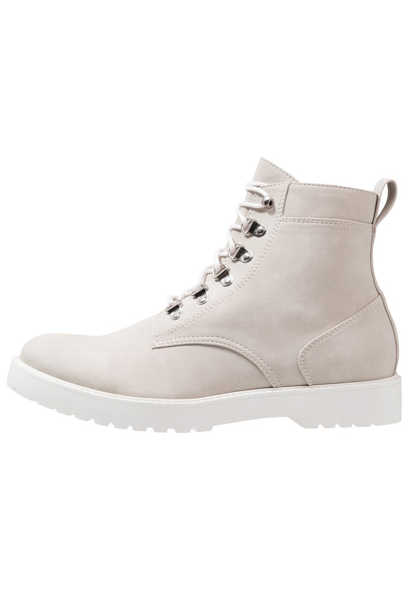 Stivaletto grigio chiaro in suede, con punta rotonda, suola in gomma bianca e occhielli metallici per i lacci. Include un anello sul retro per facilitare la calzata.