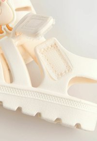 White sandal made of textured plastic, featuring an adjustable strap and a prominent sole with a patterned tread. Cute character detail visible.