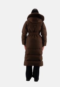 Cappotto lungo imbottito marrone con cappuccio foderato in pelliccia sintetica, vita aderente e tasche laterali. Presenta una finitura liscia e una silhouette oversize.