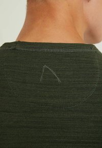 Tejido texturizado de color verde oscuro en la parte trasera de una camisa, con un escote circular y pequeños detalles de costura visibles.