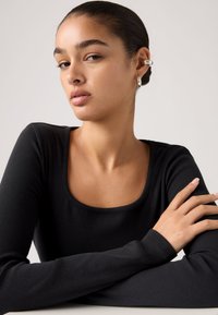 Μαύρο ριμπ ζιβάγκο με μακριά μανίκια και τετράγωνο ντεκολτέ. Λείο ύφασμα και εφαρμοστή γραμμή, σε συνδυασμό με ασημένια κρίκους σκουλαρίκια.