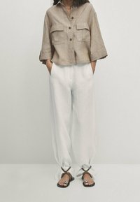 Lysebrunt linned cropped skjorte med to frontlommer, parret med løse hvide bukser og strappy sorte sandaler.