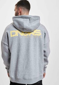 Sudadera gris con un gran gráfico amarillo que dice "DNGRS INVADER" en la parte de atrás. Cuenta con capucha ajustable y corte relajado.