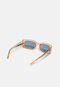 Óculos de sol quadrados com armações transparentes em pêssego e lentes em tom azul. Templos finos e angulares com um discreto detalhe de logotipo nas hastes.
