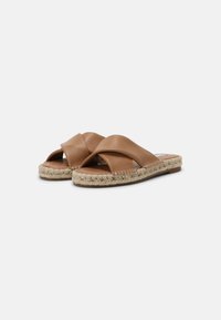 Des sandales espadrilles en cuir marron avec des semelles en jute tressé et de larges brides croisées sur fond blanc.