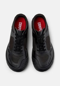 Black athletic shoes with a mesh design, featuring a thick rubber sole, black laces, and a red insole displaying the brand name.