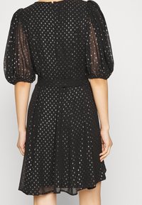 Black dress with puffed sleeves, adorned with silver dot patterns. Made of sheer fabric, cinched at the waist, with a flared skirt.
