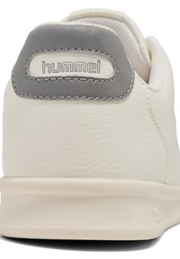 White textured sneaker with a grey heel tab featuring a stitched logo. Soft material and minimalist design with a smooth rubber sole.