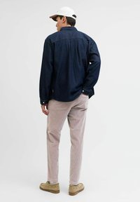 Mørkeblå denimskjorte med lange ærmer og manchetteknapper, parret med lysebeige cordbukser. En neutral kasket og afslappede sko fuldender looket.