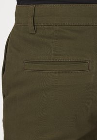 Olivgröna byxor av slitstarkt tyg, med en bakficka med sydd kant och en mjuk, slät textur.