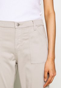 Béžové kalhoty ze směsi bavlny s předními kapsami, zapínáním na knoflík a viditelnými švy. Hladký povrch a přiléhavý střih.