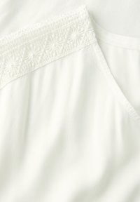 Top in tessuto bianco con dettagli in pizzo intricati vicino al colletto, texture liscia e design a vestibilità rilassata.