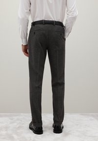 Pantaloni su misura a fantasia grigia con vestibilità dritta, cintura nera e due tasche posteriori, abbinati a scarpe nere.