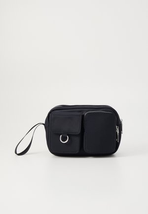 Μαύρη νάιλον τσάντα με κύριο διαμέρισμα με φερμουάρ, δύο μπροστινές τσέπες, λεπτομέρεια από ασημί δαχτυλίδι και κοντό λουρί καρπού. Λείος υφή.