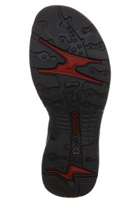 Black rubber shoe sole with textured surface, featuring a red accent design. Notable tread patterns for grip and stability.