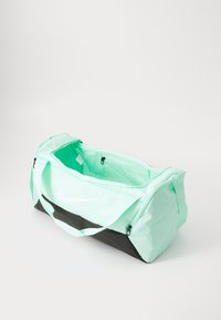 Lichtgroene sporttas met zwarte bodem, gemaakt van nylon, voorzien van een bovenste rits sluiting, korte handvatten en een wit logo op de zijkant. Breedte: ongeveer 60 cm.