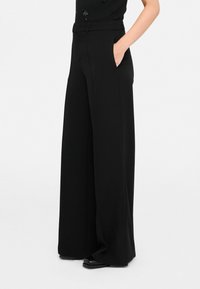 Pantaloni neri a gamba larga con una texture liscia, dotati di vita alta e tasche laterali, progettati per un fit rilassato.