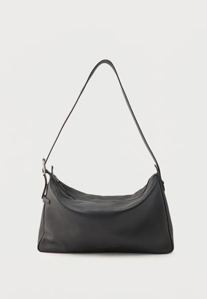 Musta nahkainen olkalaukku, jossa kaareva ylävetoketju ja ohut säädettävä hihna yksiväristä vaaleaa taustaa vasten.