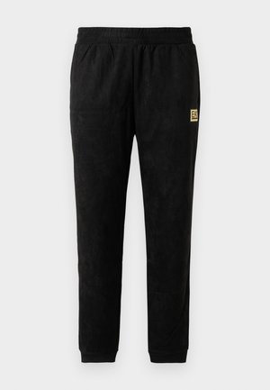 Pantalones jogger de velour negro con cintura elástica, tobillos con puños, bolsillos laterales y pequeño parche del logo beige EA7 Emporio Armani en el muslo.