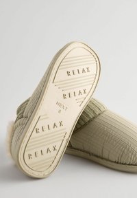 Grøn strikket hjemmesko med beige gummi sål. Sålen har ordet "RELAX" og teksturerede linjer. Overdelen er blød med et ribbet mønster.