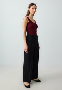 Bordeaux geribbelde tanktop gecombineerd met een zwarte broek met wijde pijpen en zwarte flats. Soepele textuur, getailleerde top, vloeiende broek met een lange lengte.