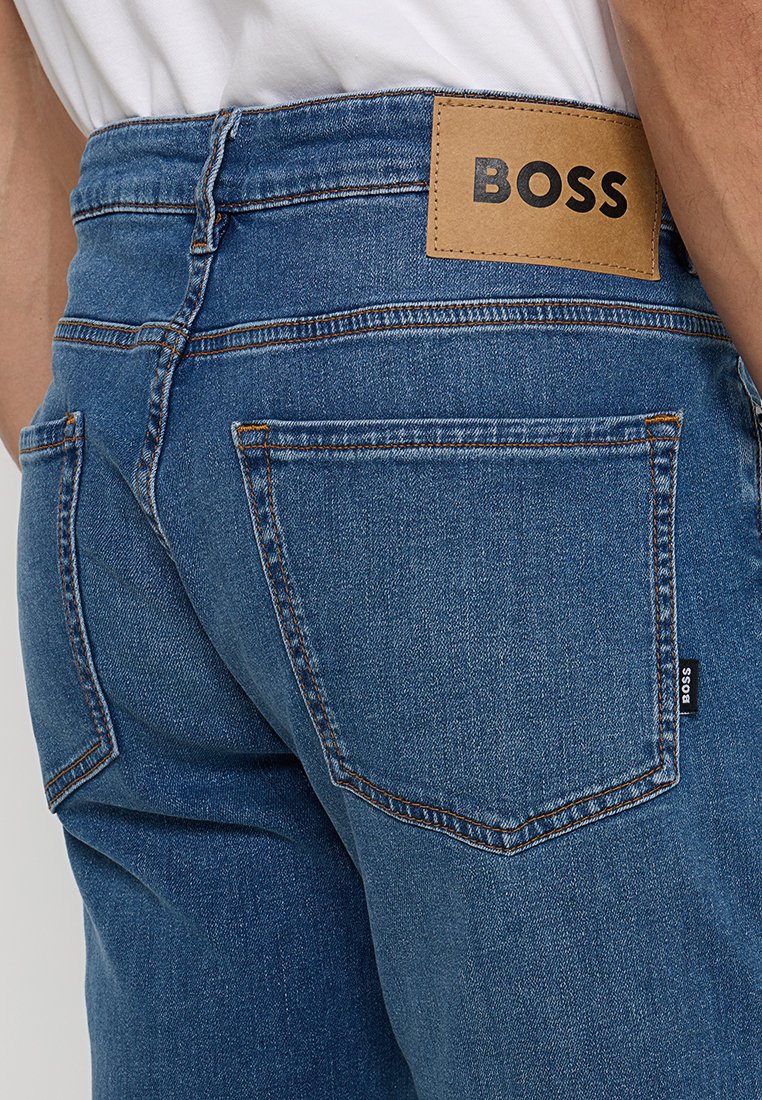 Niebieskie dżinsy z denimu z brązową skórzaną naszywką z logo "BOSS", widocznym przeszyciem oraz dwoma tylnymi kieszeniami z subtelnymi detalami.