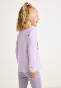 Lavendel langærmet skjorte med rund halsudskæring og et farverigt grafisk print på forsiden, parret med lys lilla teksturerede leggings.