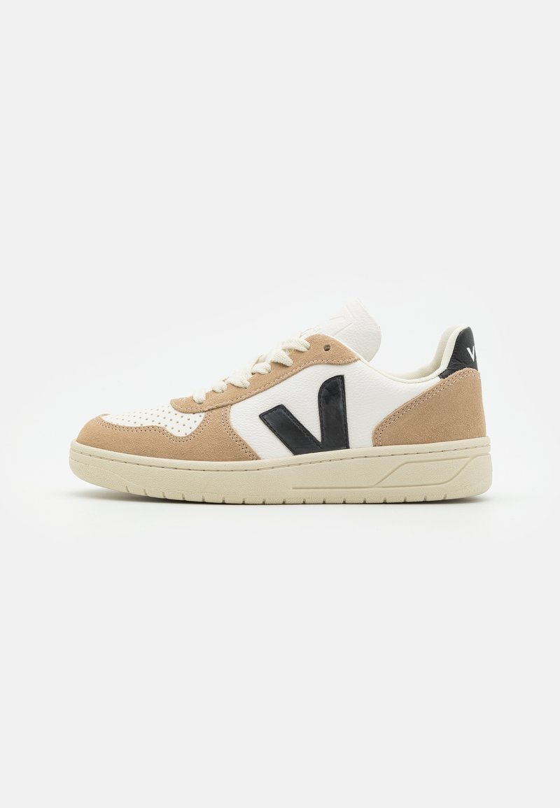 Low-top sneaker with beige suede overlays, white leather panels, cream sole, black "V" logo on side, and white laces on a white background.
