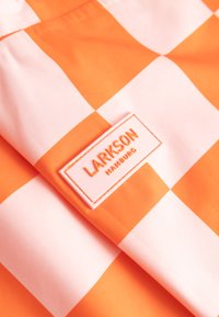 Oranžovo-bílá kostkovaná látka s přišitou obdélníkovou štítkem s nápisem "LARKSON HAMBURG" v oranžových písmenách.