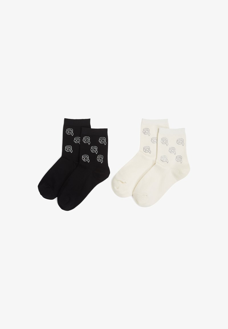 Calcetines de tobillo en negro y crema, con un diseño gráfico repetido. El par negro tiene un fondo oscuro con motivos grises; el par crema tiene un fondo claro.