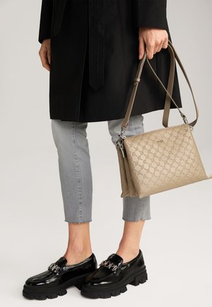 Mocassini neri in vernice con suola spessa, jeans grigi a vita corta e una borsa beige con motivo e tracolla.