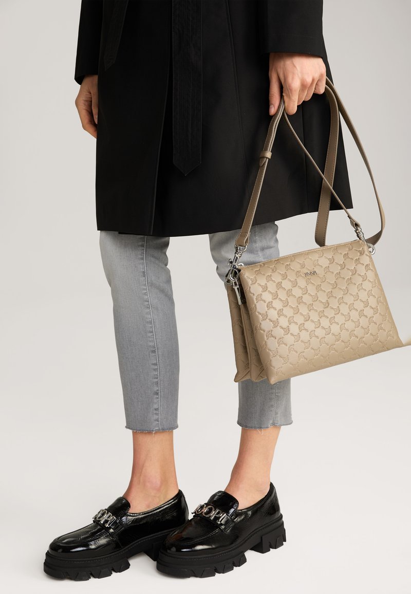 Mocassini neri in vernice con suola spessa, jeans grigi a vita corta e una borsa beige con motivo e tracolla.