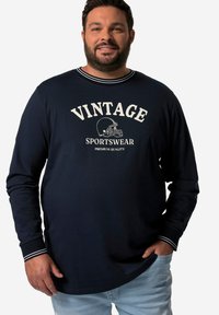 Granatowa koszulka z długim rękawem z białym nadrukiem "VINTAGE SPORTSWEAR". Posiada kontrastowe pasek przy dekolcie i mankietach, gładką fakturę materiału.