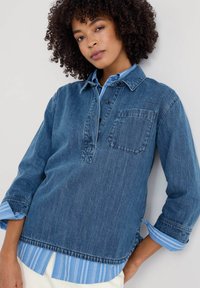 Dunkelblaue Jeanshemd mit Knopfleiste, einer aufgesetzten Tasche und sichtbaren, schichtweise angeordneten, hellblauen gestreiften Manschetten an den Ärmeln.