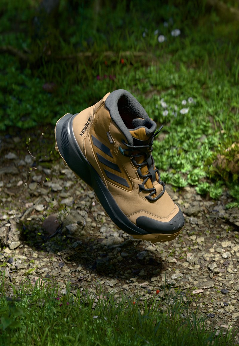 Brązowe buty trekkingowe z teksturowaną powierzchnią, czarnymi akcentami i sznurówkami. Zaprojektowane do użycia na świeżym powietrzu, z wyściełanym kołnierzem i gumową podeszwą.