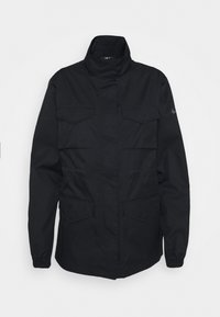 Svart arbetarskjorta med hög krage, dragkedjestängning, två bröstfickor och elastiska ärmslut. Tillverkad av slitstarkt, texturerat tyg.